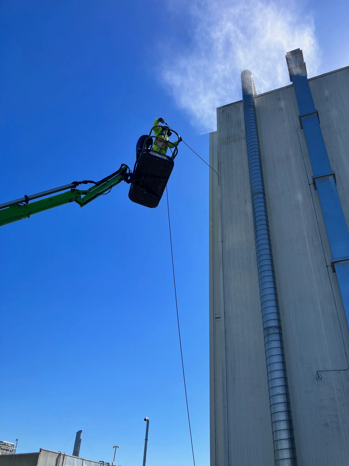 Technician in a boom lift cleaning a multi-storey commercial building with industrial ducting