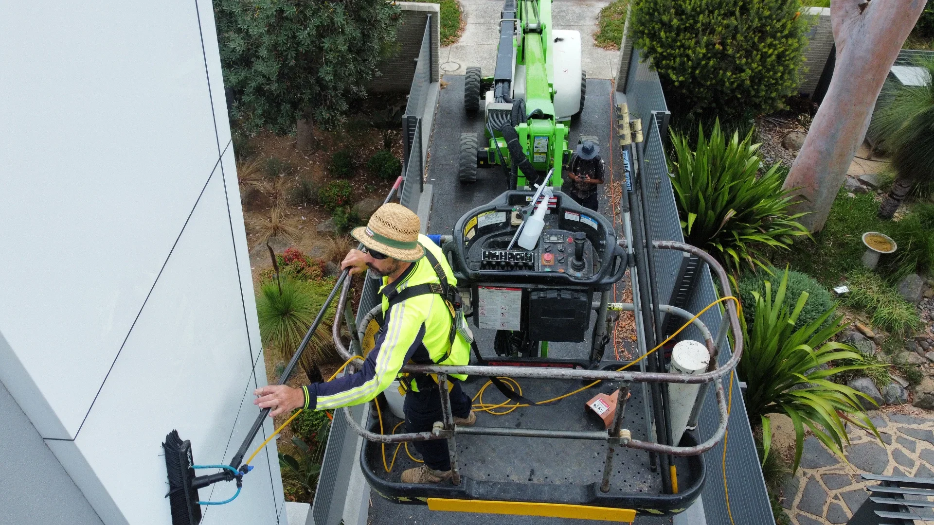 Technician soft-washing a render wall from a boom lift