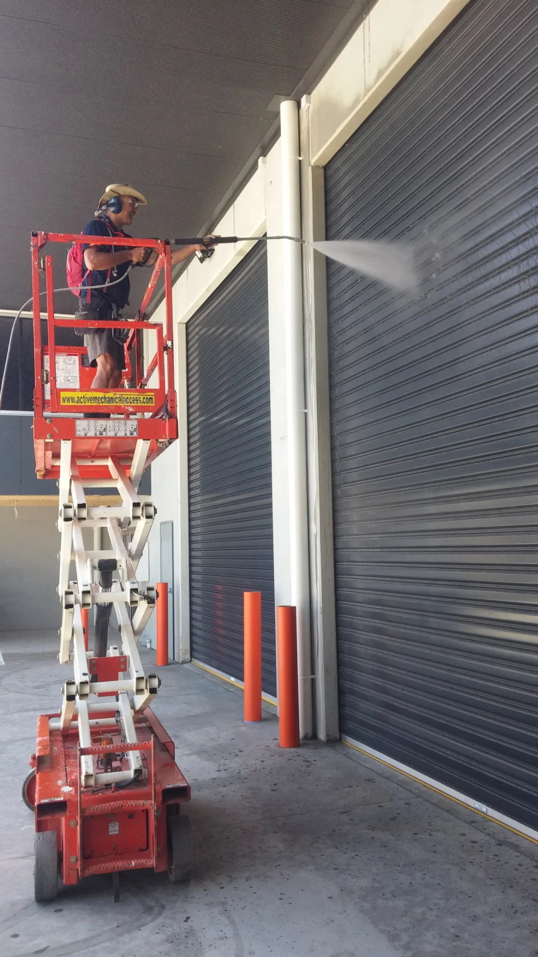 Technician on a scissor lift pressure washing an industrial unit exterior