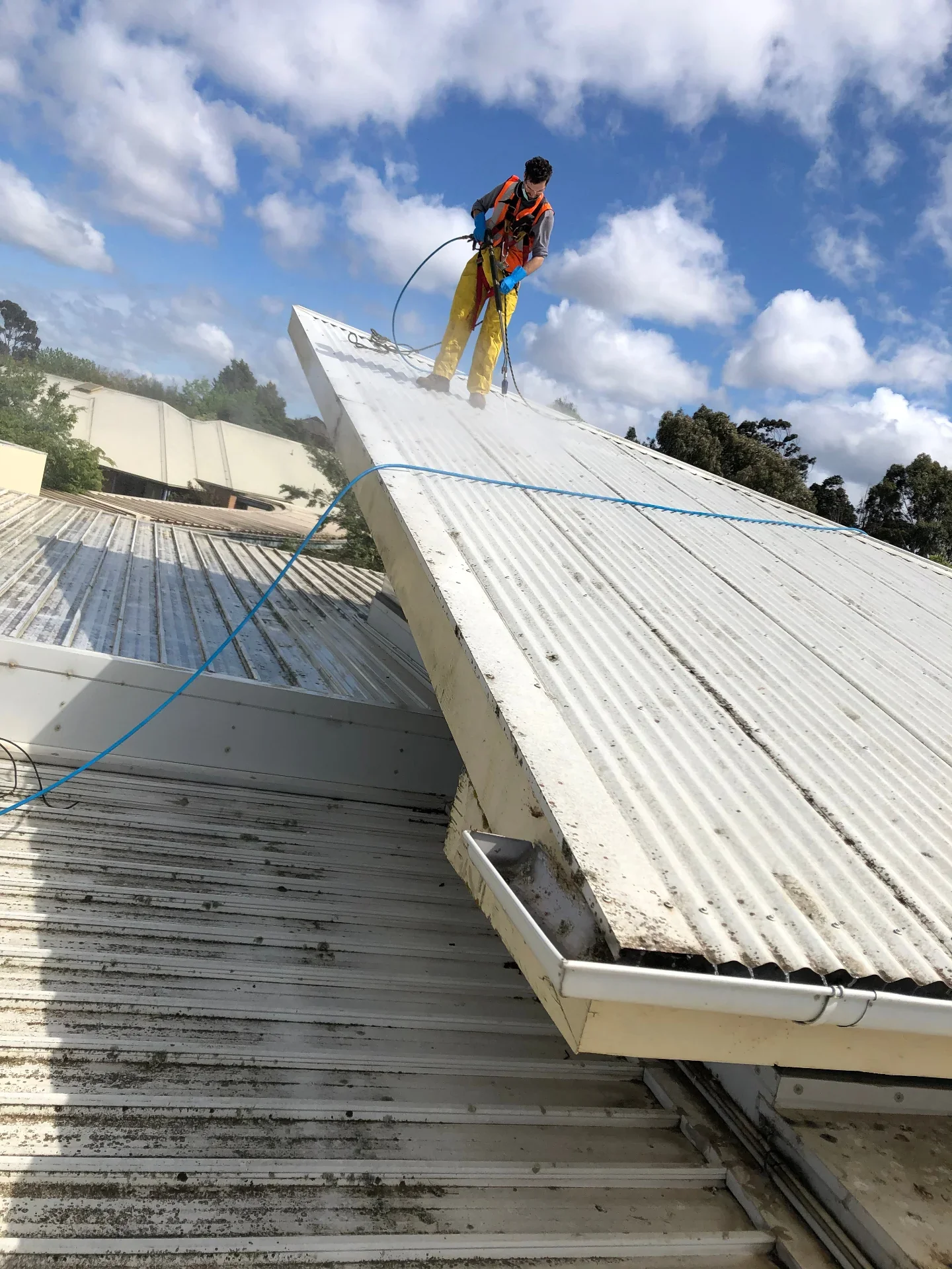 Technician harnessed on a pitched roof soft-washing panels