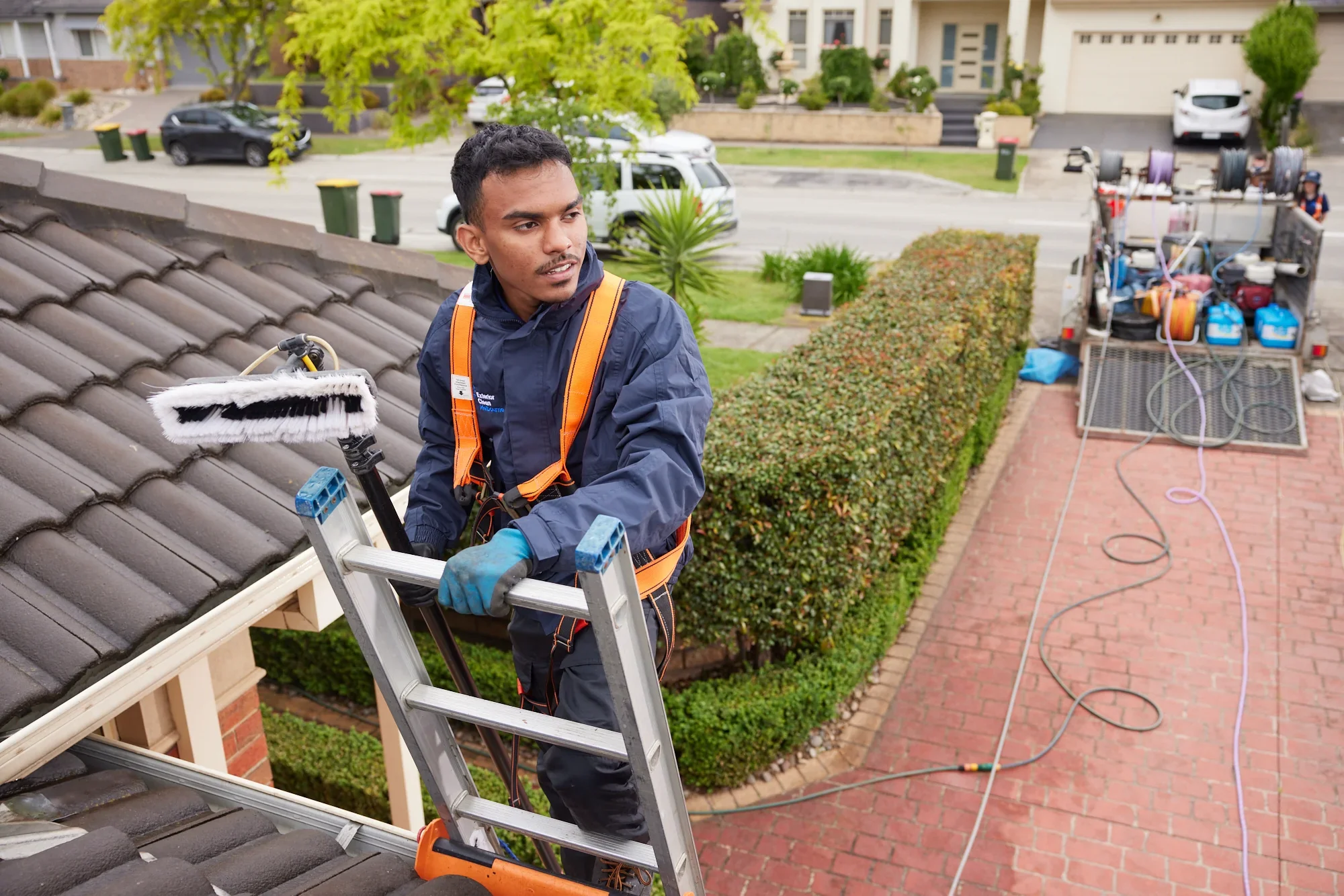 Technician on a ladder cleaning gutters with a water-fed pole