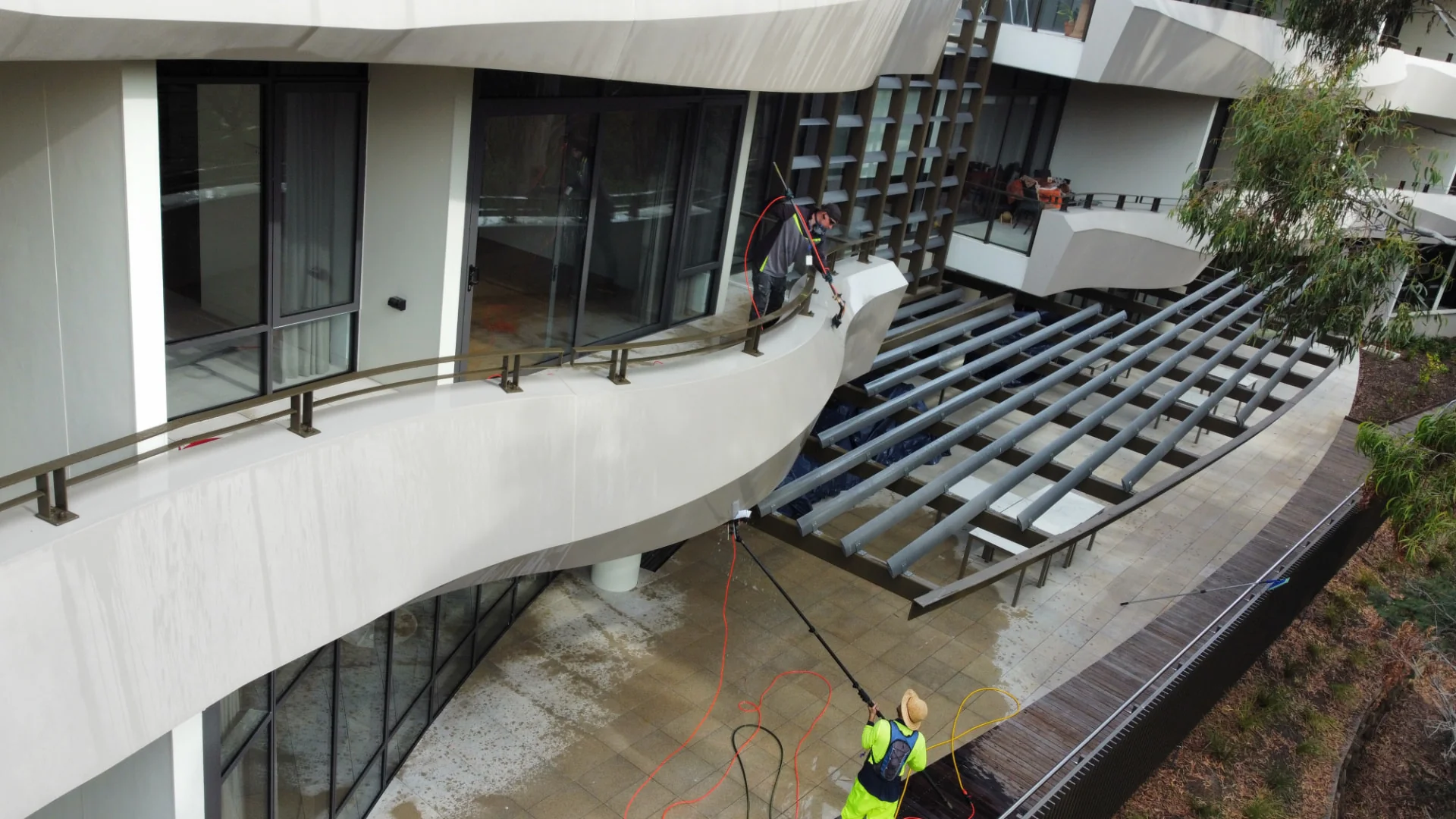 Technicians cleaning a modern multi-storey strata balcony with water-fed poles
